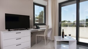 Una habitación moderna con televisión de pantalla plana, un escritorio, una silla y una pequeña mesa con copas de vino y una botella.