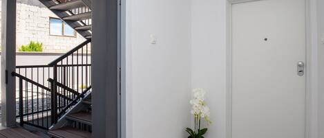 A staircase leading to an outdoor area with a white door and a potted orchid.
