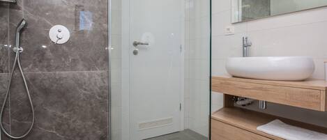 Un baño moderno con cabina de ducha de vidrio, un lavamanos blanco y un mueble de tocador de madera.