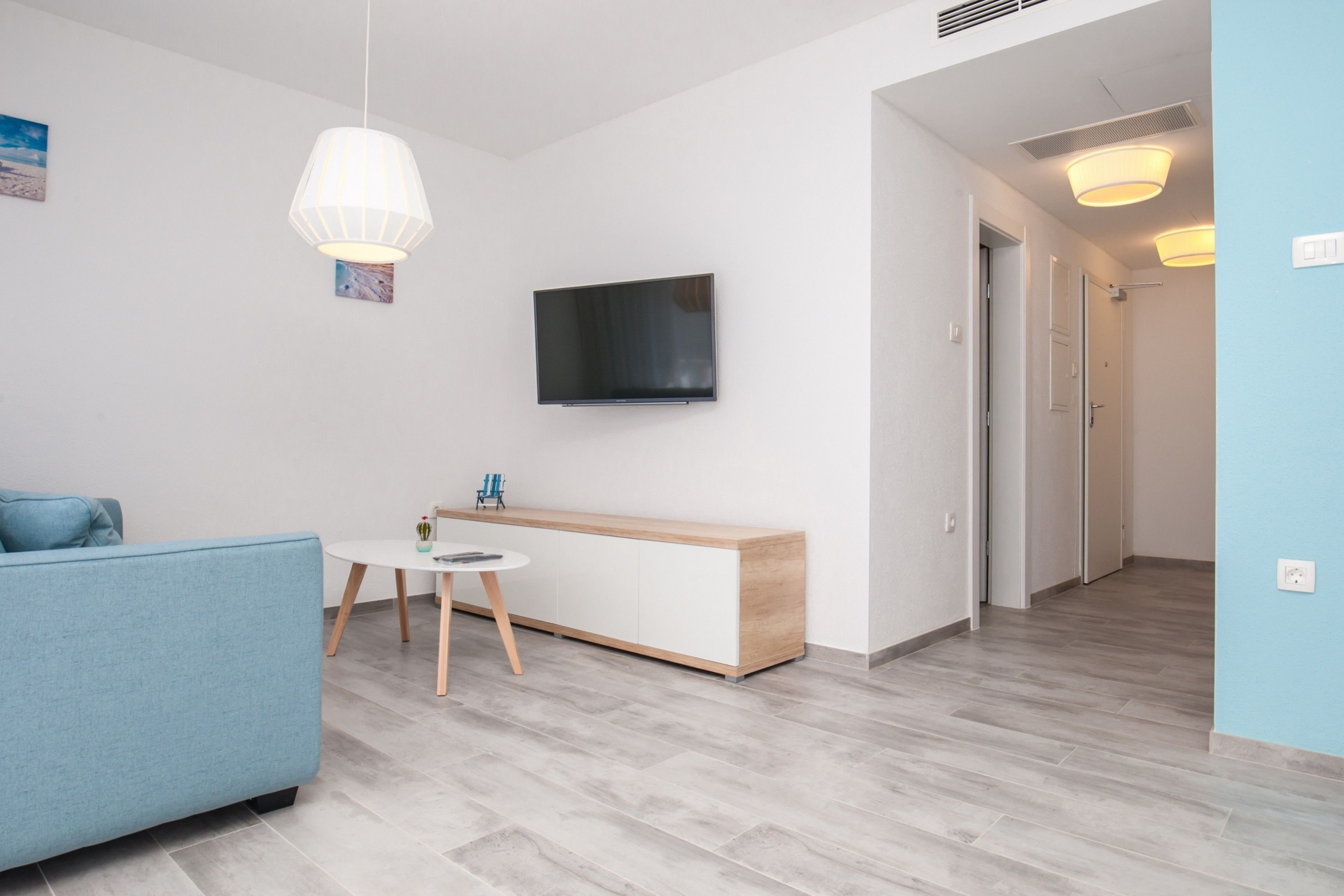 Ein modernes Wohnzimmer mit einem blauen Sofa, einem Holzkonsolentisch, einem kleinen runden Tisch und einem wandmontierten Flachbildfernseher.