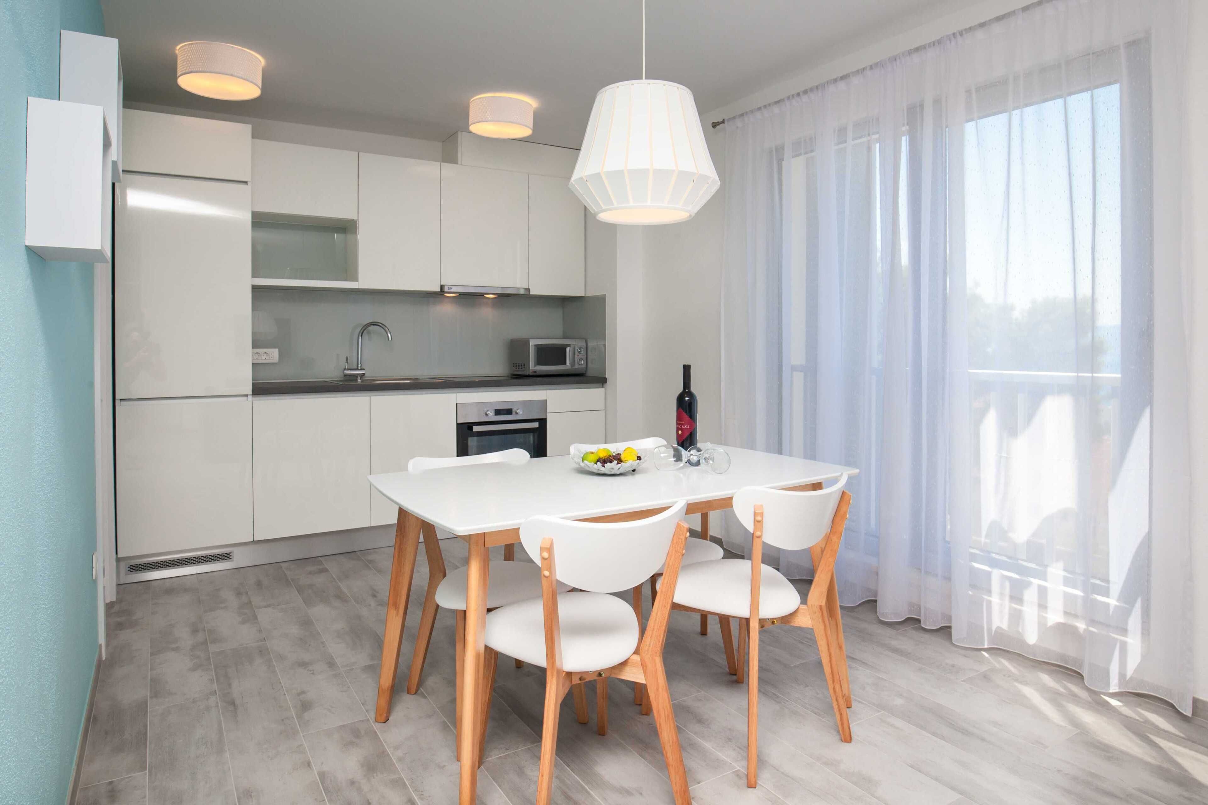 Cozinha moderna com armários brancos, uma mesa de jantar com cadeiras, um micro-ondas e uma garrafa de vinho sobre a mesa.