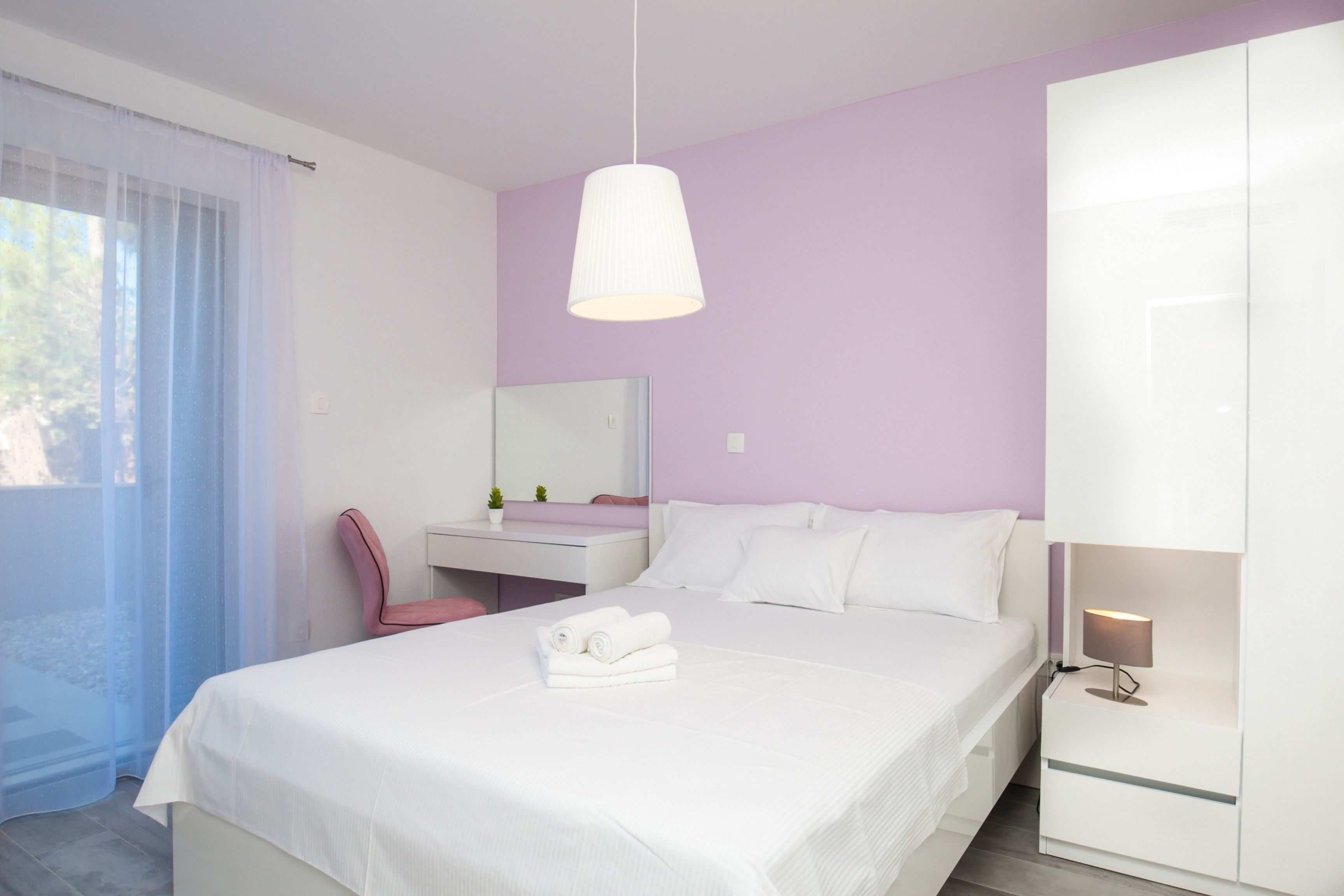 A modern bedroom with a bed, a bedside table with a lamp, a vanity with a mirror, and a chair.
