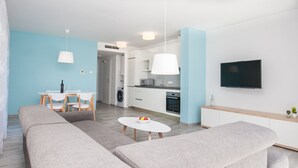 A modern living room with a sofa set, a dining table with chairs, a kitchen area with a microwave, and a TV mounted on the wall. - Apartments Dva Galeba (Bol)