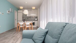 A modern living room with a grey sofa, a dining area with white chairs, and a kitchen with white cabinets and a white ceiling light. - Apartments Dva Galeba (Bol)