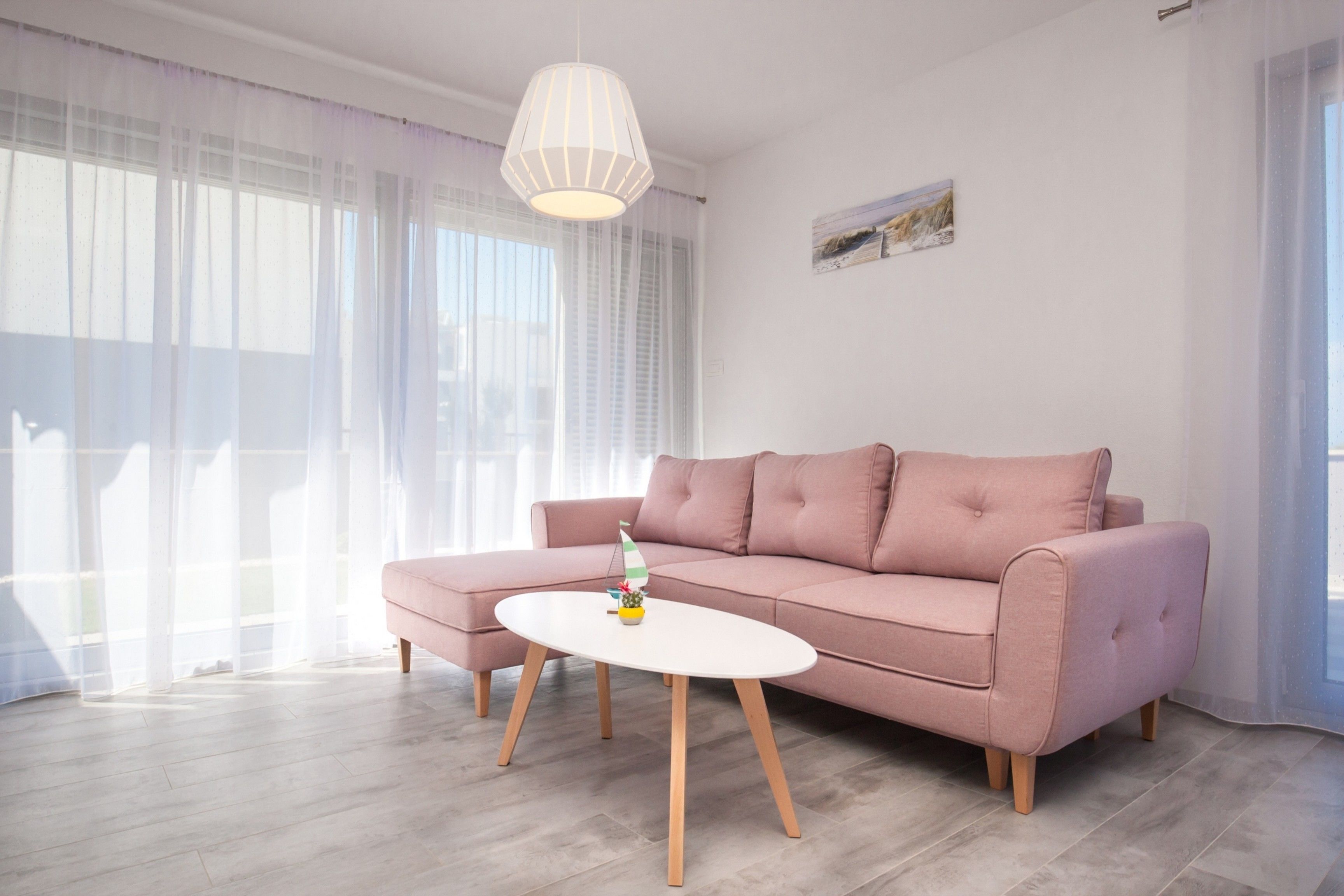 A modern living room with a pink sofa, a white coffee table, and sheer curtains.