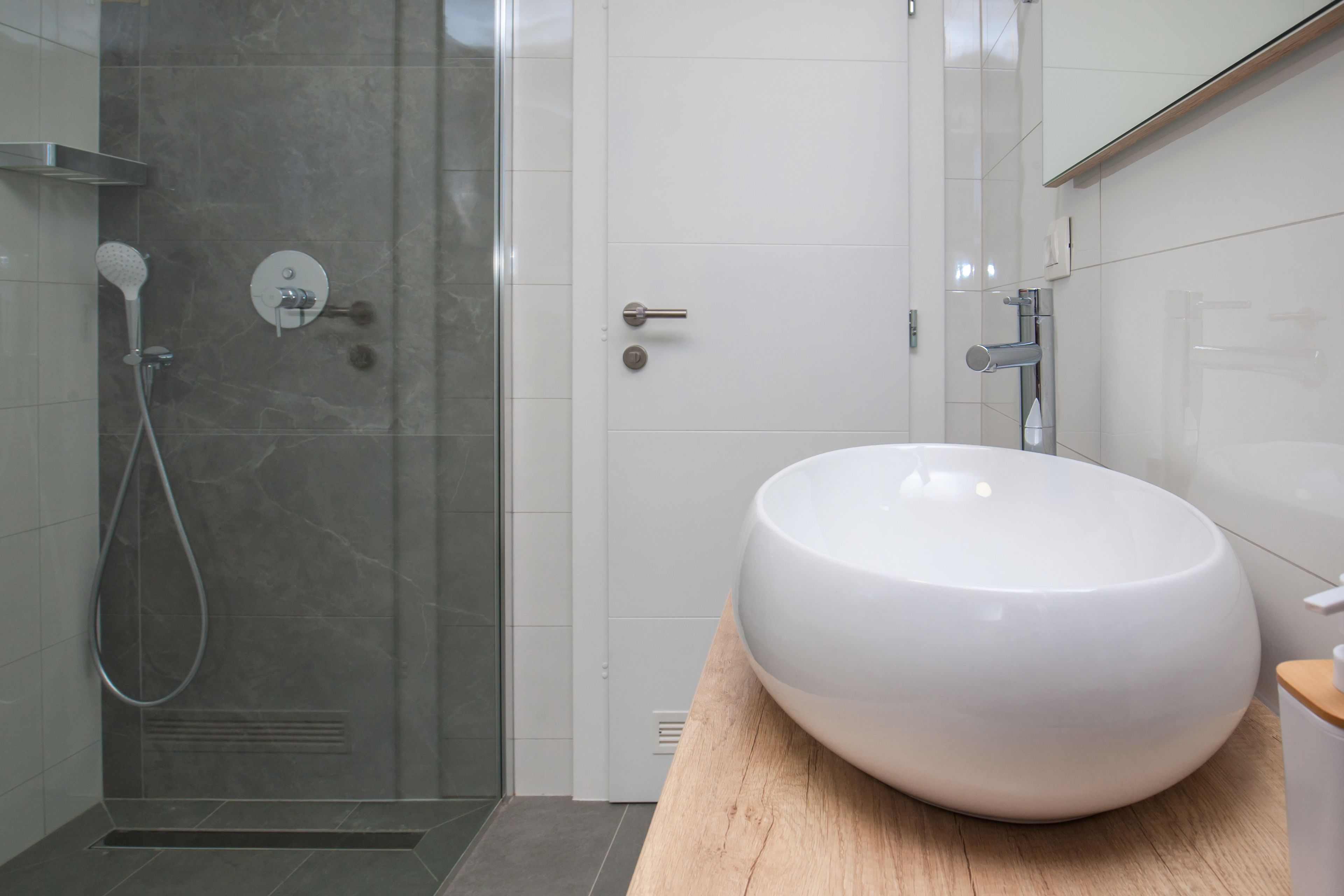 Ein modernes Badezimmer mit einem großen, weißen Waschbecken, einer Glasdusche und einer Holzauslage.