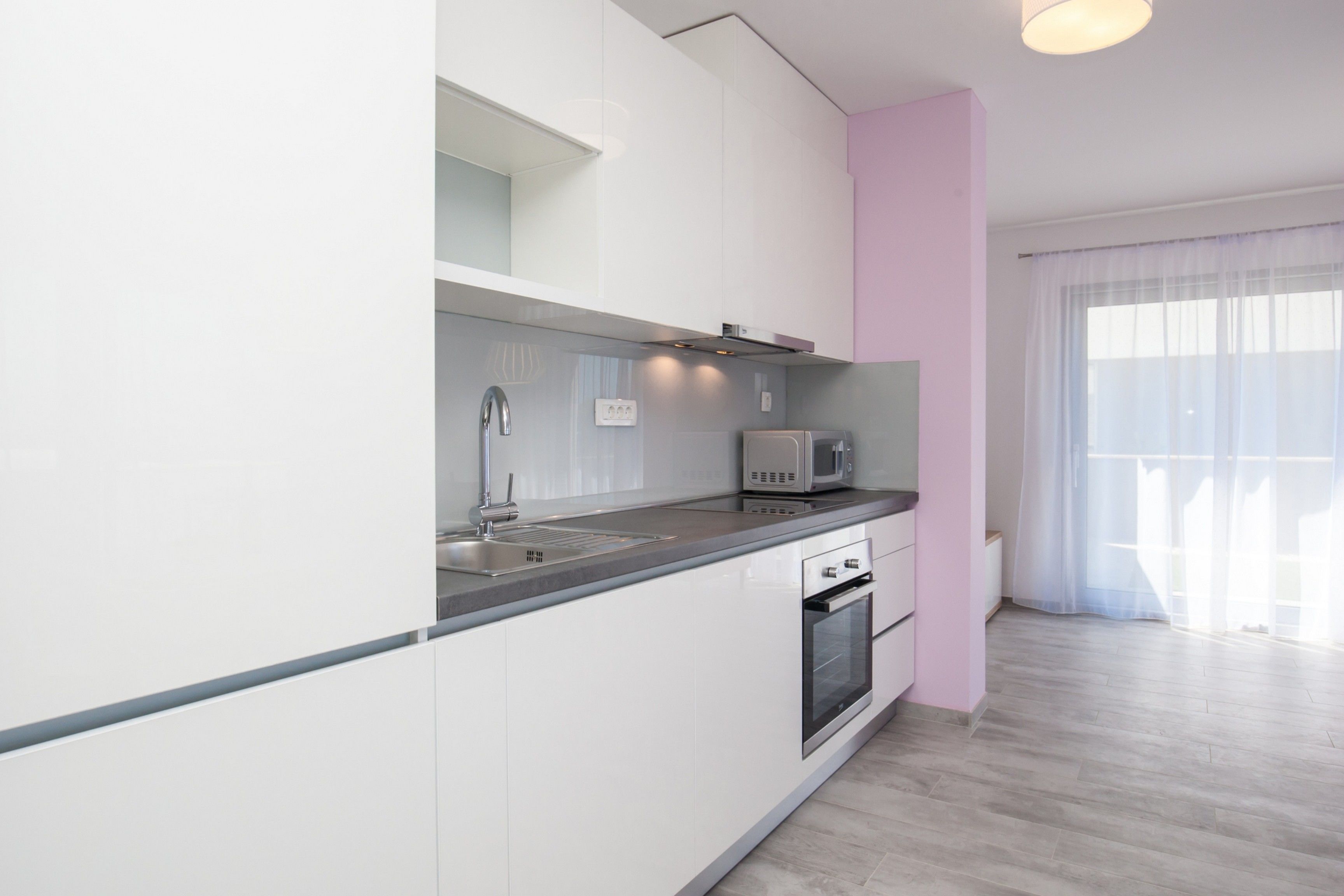 A modern kitchen with white cabinets, a stainless steel sink, a microwave, and an oven.