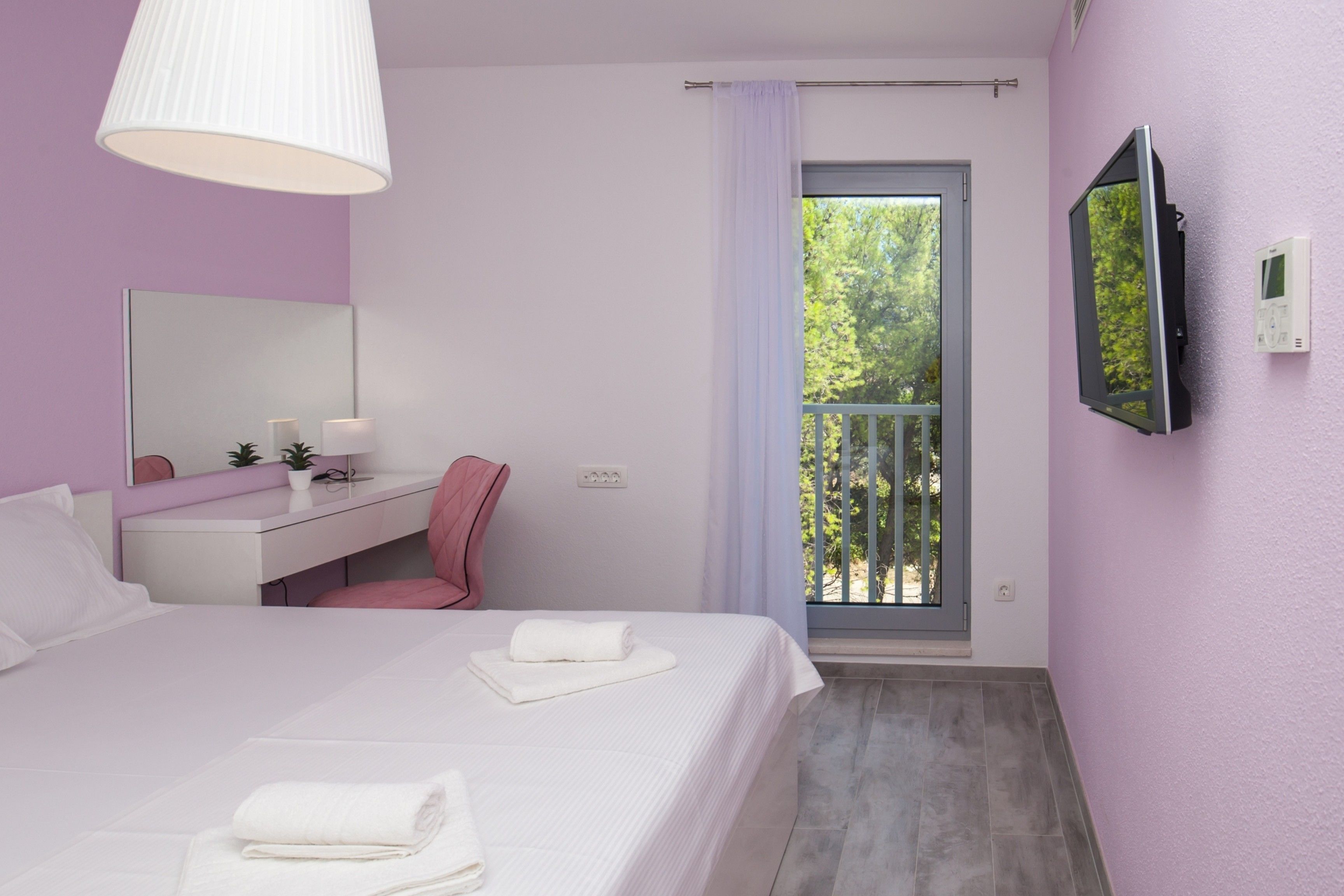 Une chambre à coucher comprenant un lit, une table de chevet, un miroir, une fenêtre donnant sur des arbres et un téléviseur fixé au mur.