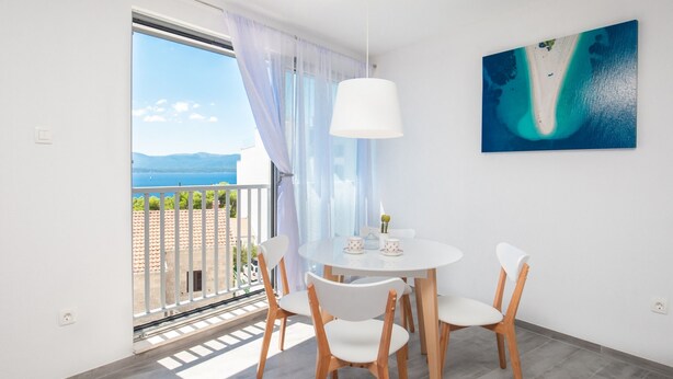 A room with a round table, white chairs, a ceiling light, a view through a sliding door, and a painting on the wall. - Apartments Dva Galeba (Bol)