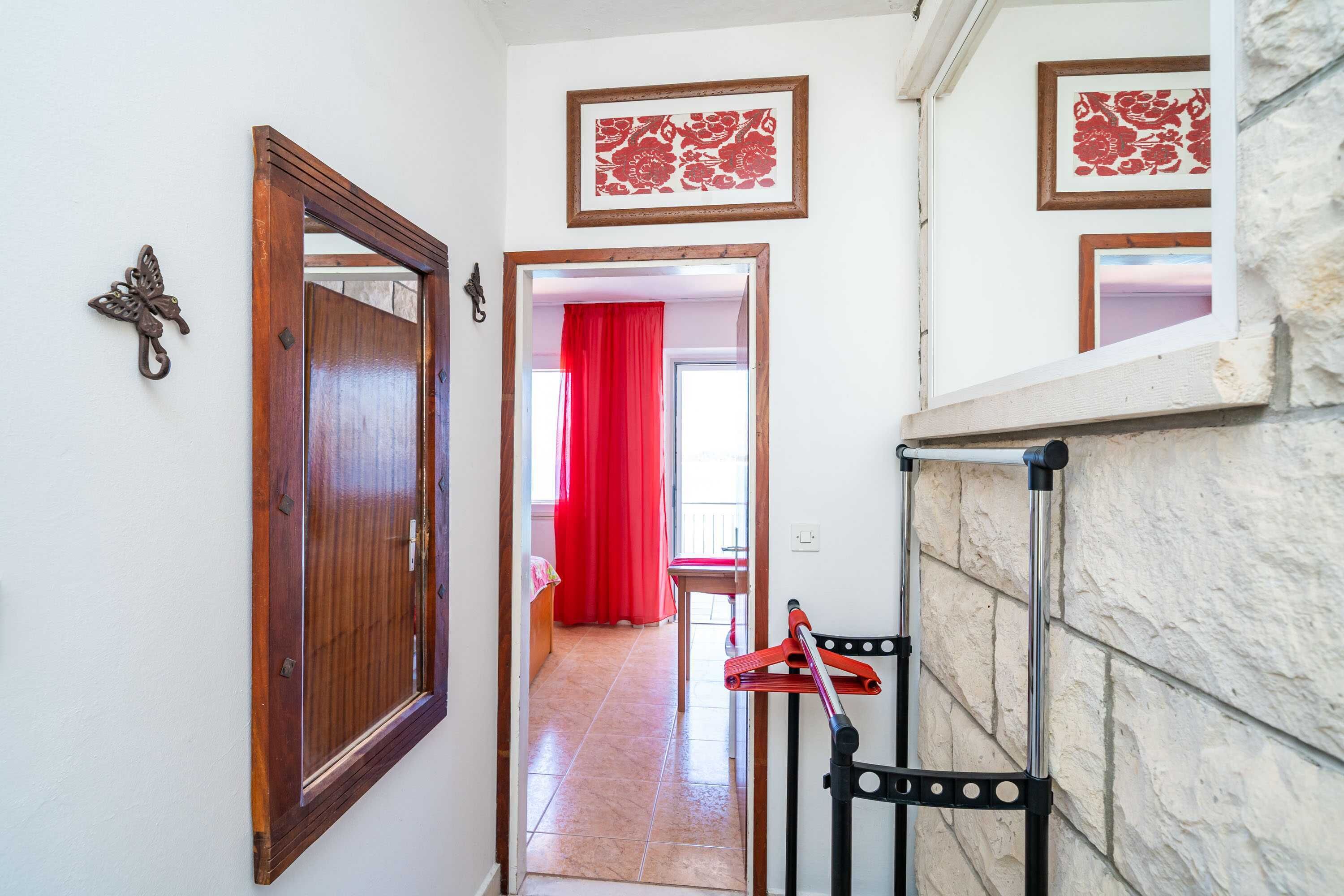 Un pasillo con puerta de madera, cortina roja y silla de metal.