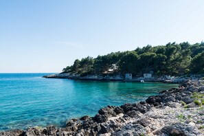 A coastal landscape with rocky terrain, clear turquoise water, and a small building on a hill. - VENUS PALACE Golden Gate rooms (Lumbarda)