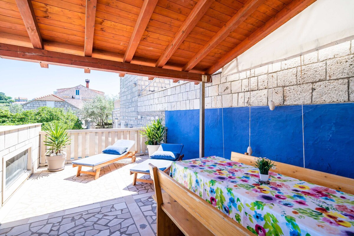 An outdoor patio with wooden furniture, a table with a floral tablecloth, and a view of the cityscape.