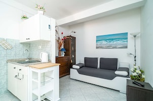 Un espacio habitable compacto con kitchenette, un sofá, un cuadro y una lámpara.