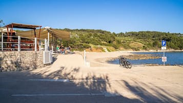 Eine Küstenstraße mit einer Steinmauer, einer überdachten Sitzgelegenheit und freiem Blick auf das Meer.