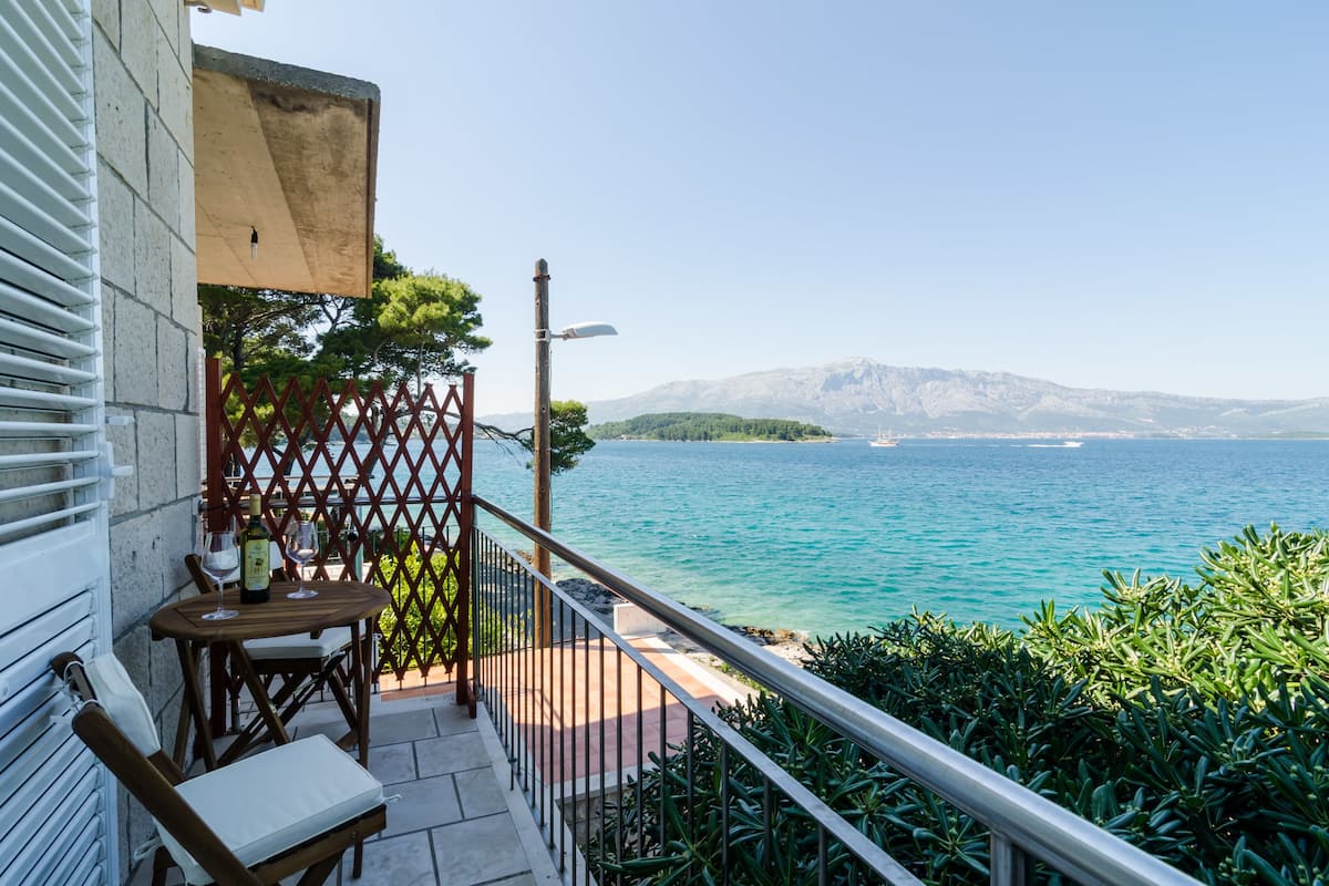 Een balkon met een tafel en stoelen, met uitzicht op zee en bergen op de achtergrond.