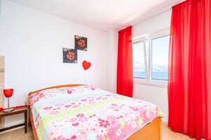 Un dormitorio con una cama, un ventanal con cortinas rojas y dos obras de arte colgadas en la pared.