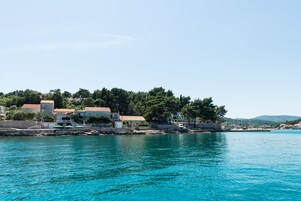 Un pueblo costero con edificios a lo largo del frente marítimo, agua azul cristalina y un paisaje montañoso al fondo.