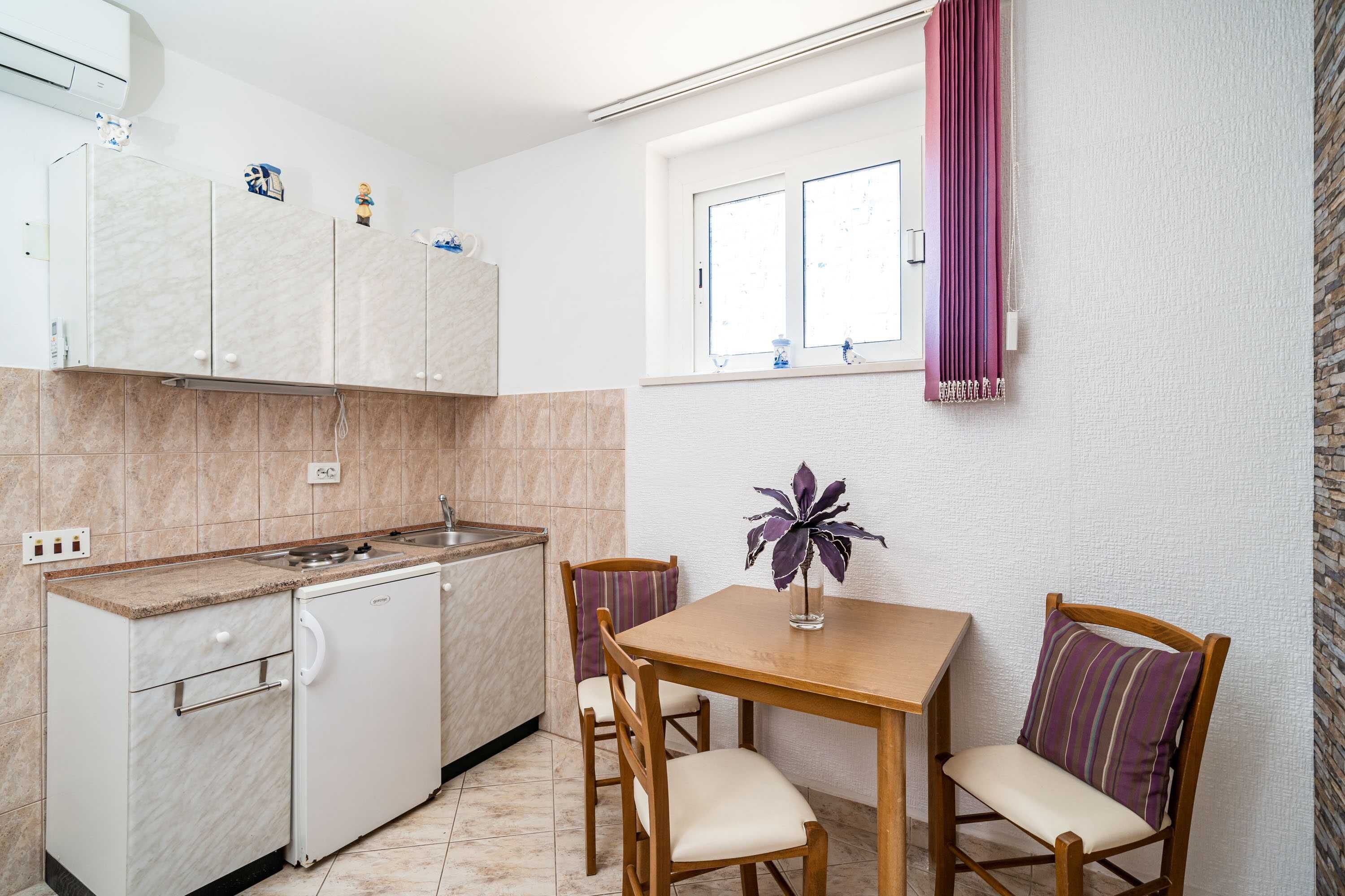 Eine kleine Küche mit einem eingebauten Geschirrspüler, einem Esstisch für zwei Personen und einem Fenster mit violetten Vorhängen.