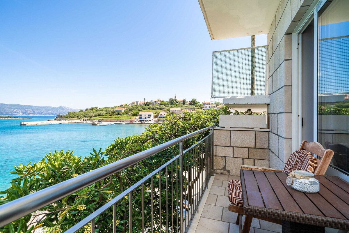 A balcony with a view of the sea, a table with chairs, and a building with a glass facade.