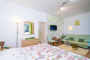 Un dormitorio con cama, cómoda, espejo, televisor y un sofá verde.