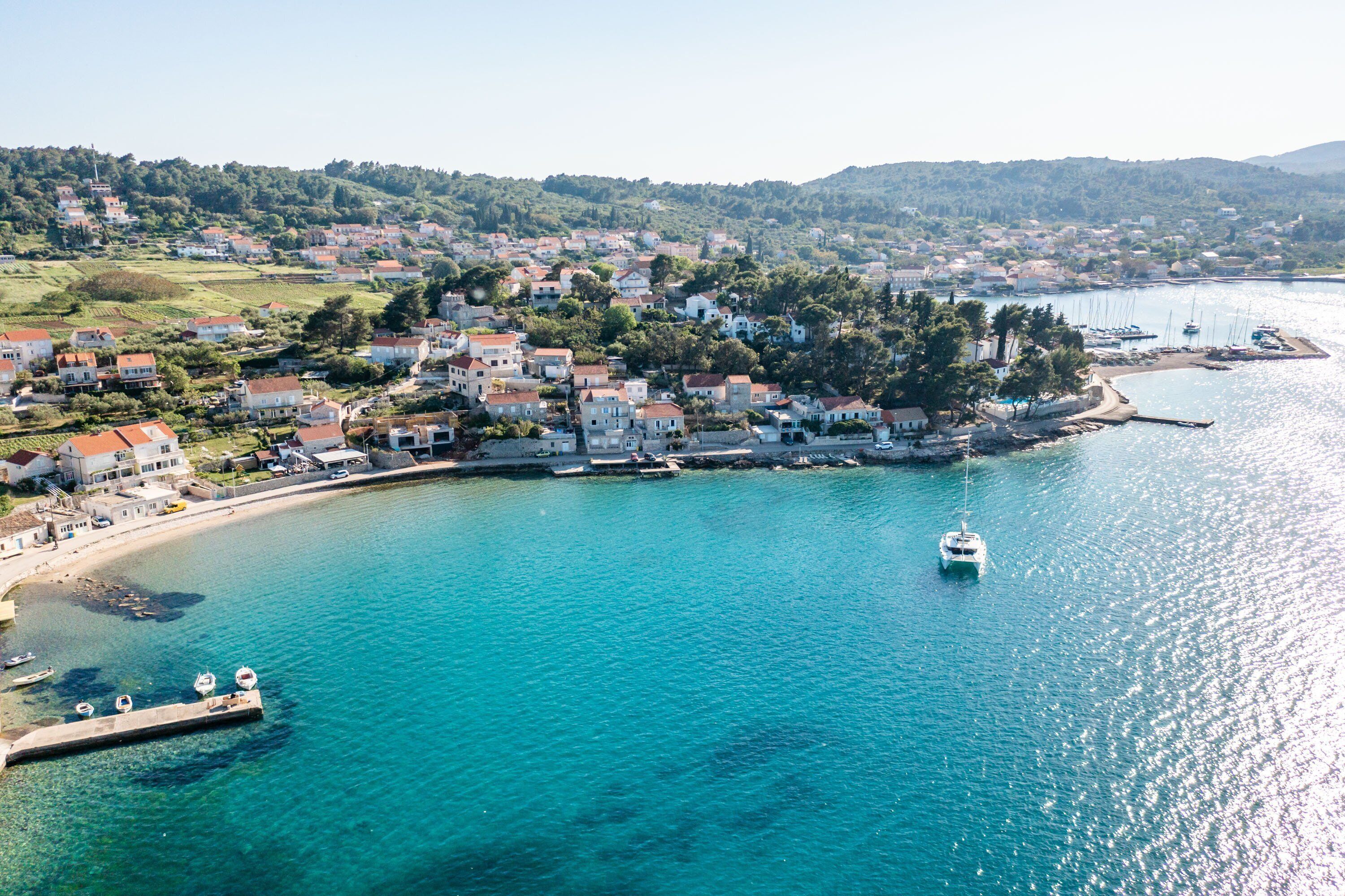 A coastal town with buildings along the waterfront, a clear blue sea, and a boat in the water.