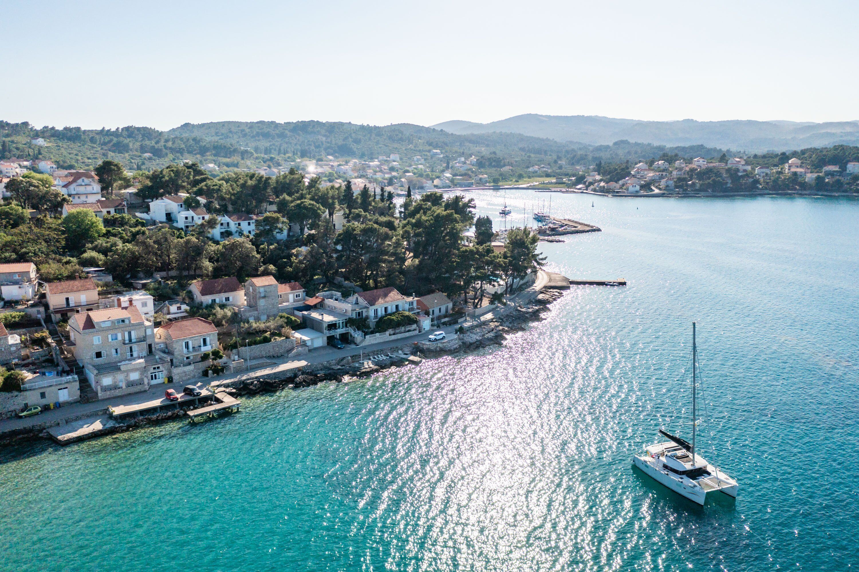 A coastal town with buildings along the waterfront, a marina with boats, and a clear view of the sea.