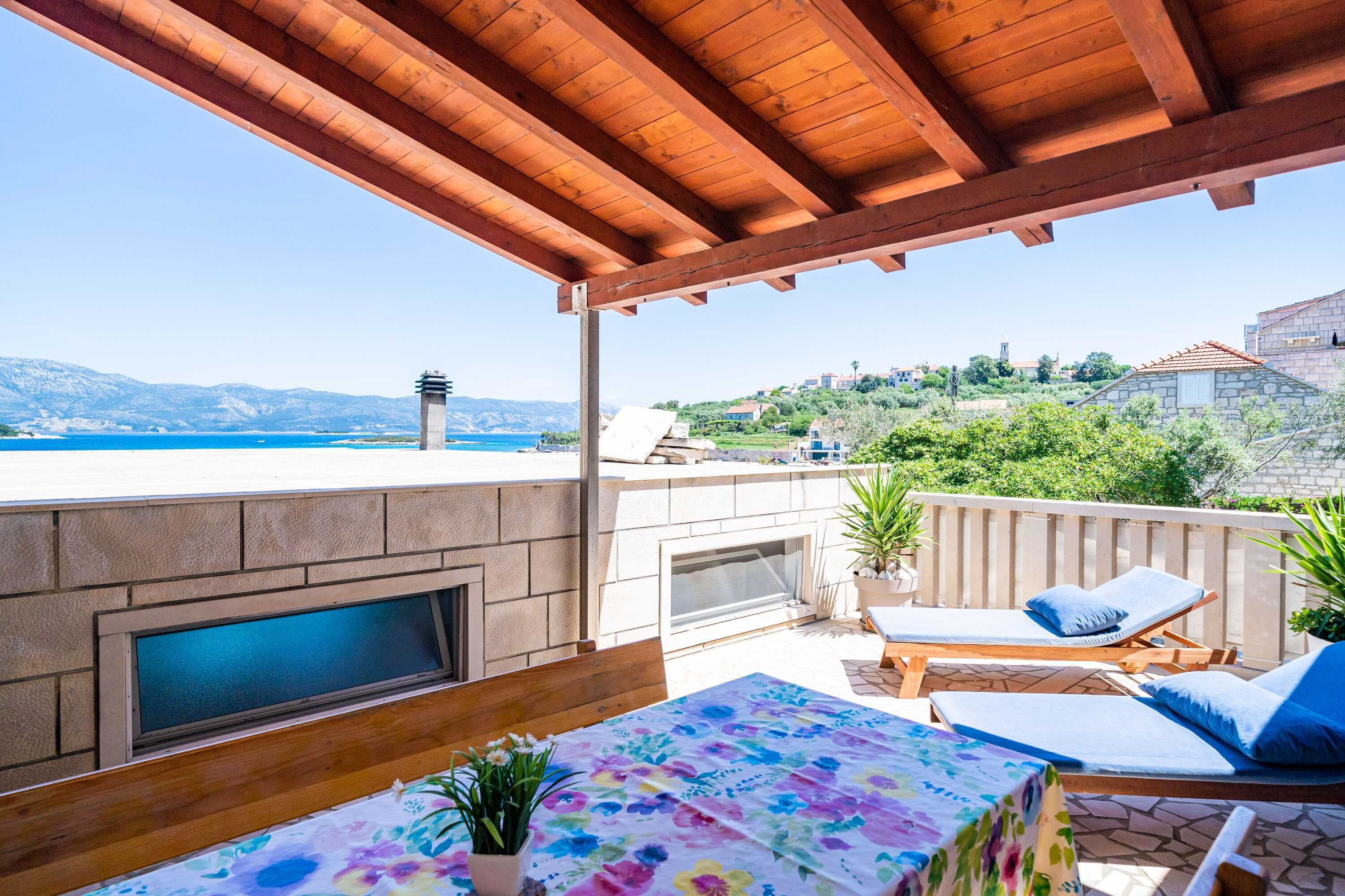 Una terrazza con vista sul mare, un muro in pietra, un barbecue, poltrone relax e un tavolo con tovaglia a fiori.