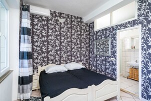 Un dormitorio con cama, una ventana y un baño visible a través de una puerta abierta.
