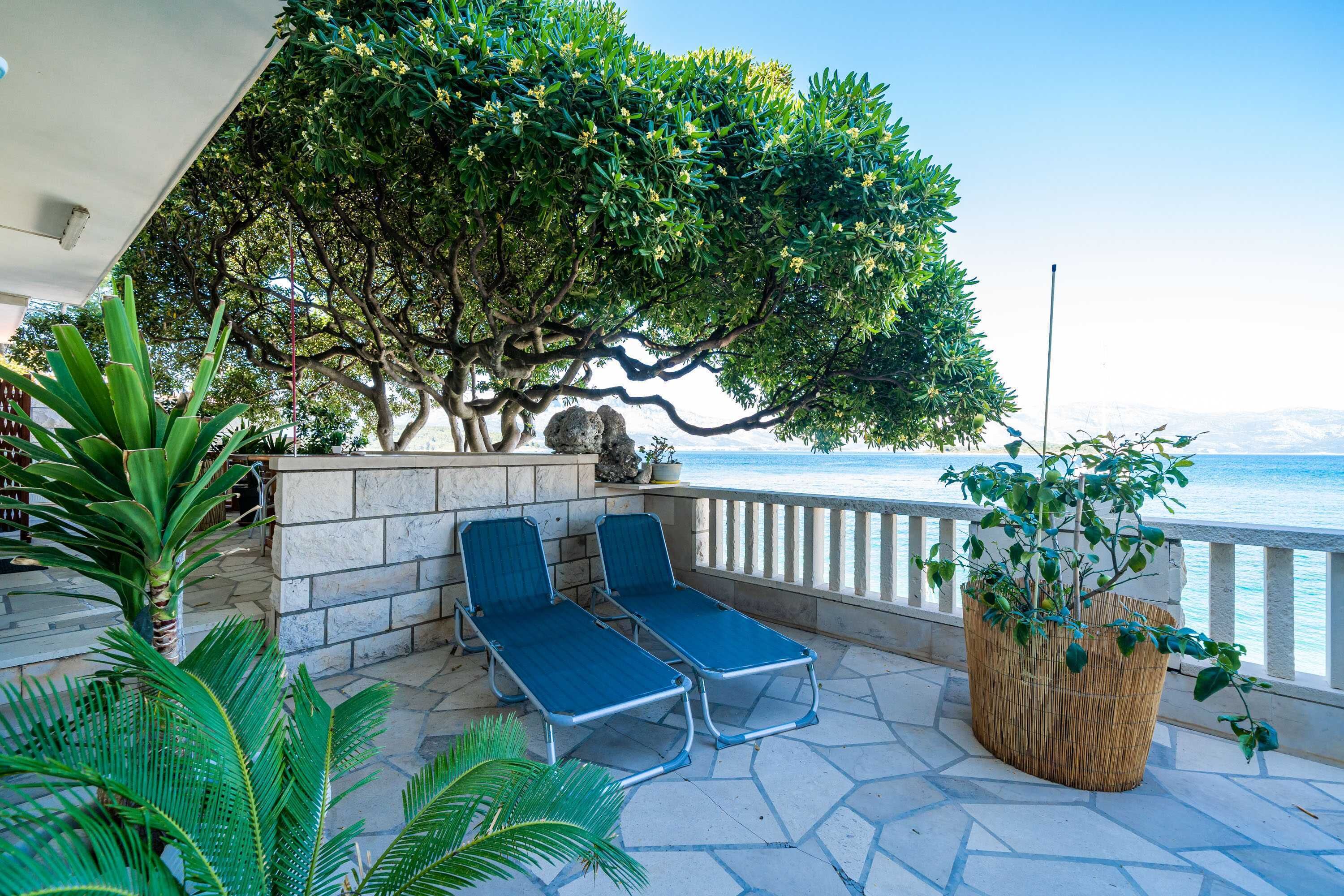A terrace with two lounge chairs, a stone wall, and a view of the sea.