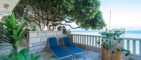 A terrace with two lounge chairs, a stone wall, and a view of the sea.