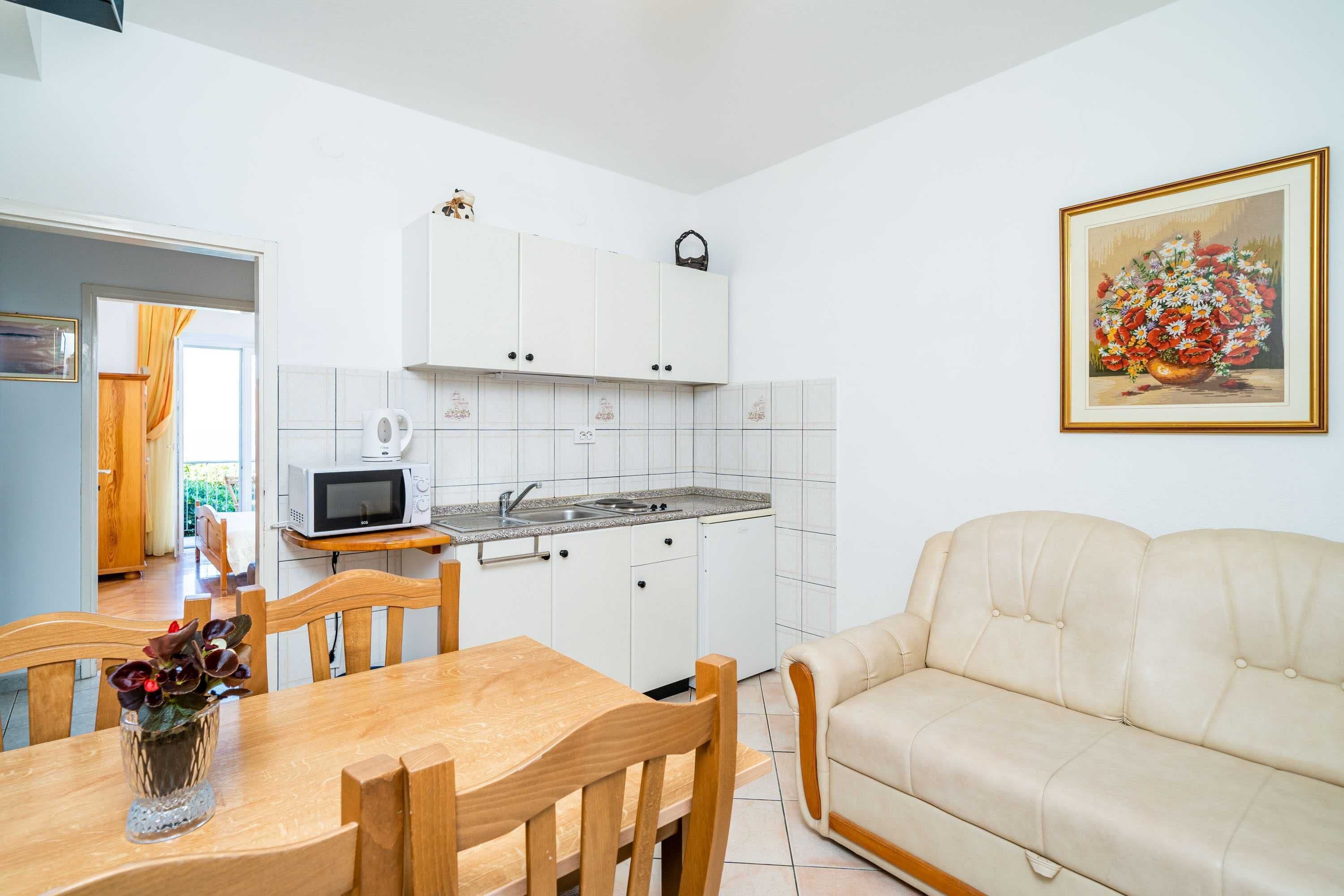 A compact kitchen with white cabinets, a microwave, and a sink. There's a dining table with chairs and a cream-colored sofa.