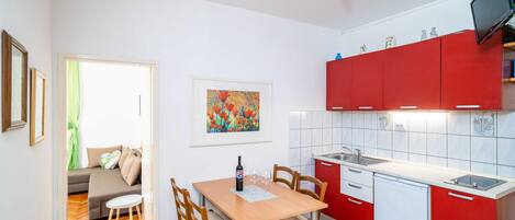 Une cuisine de taille réduite avec des meubles rouges, un coin repas comprenant une table et des chaises, et un espace de vie avec un canapé et un tableau.