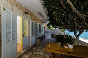 An outdoor patio with stone flooring, a wooden table, and a view of the sea. - VENUS PALACE Golden Gate rooms (Lumbarda)
