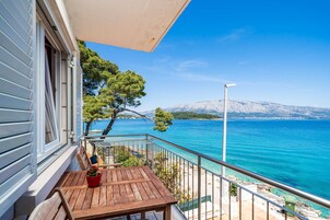 Un balcón con una mesa y sillas de madera, con vista a un mar azul y una montaña nevada en la lejanía.