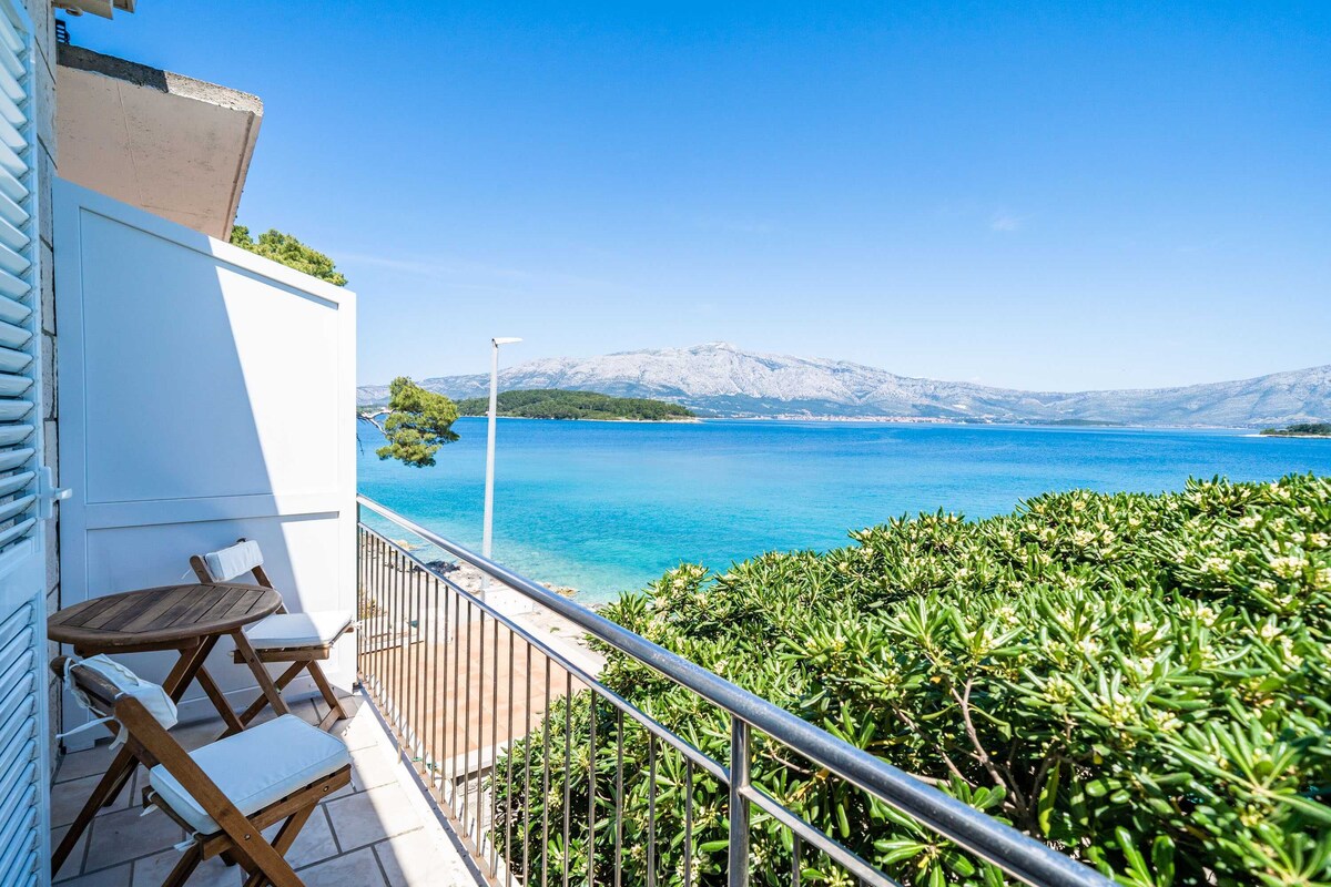 A balcony with a view of a clear blue sea and distant mountains.
