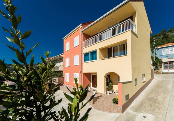 A two-story building with a balcony on the upper floor, a small entrance with steps, and a clear sky.