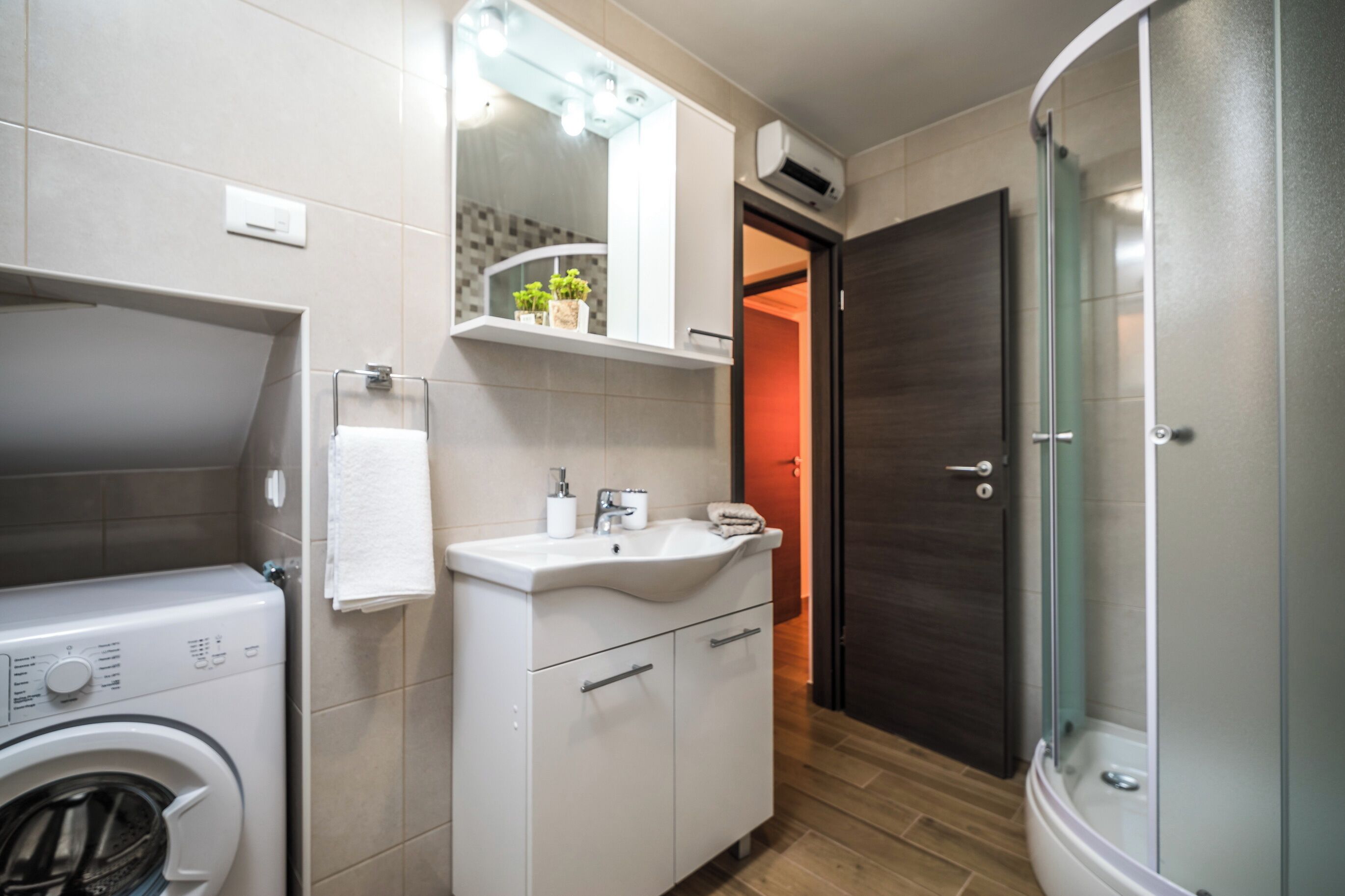 A modern bathroom with a washing machine, a sink, and a shower.