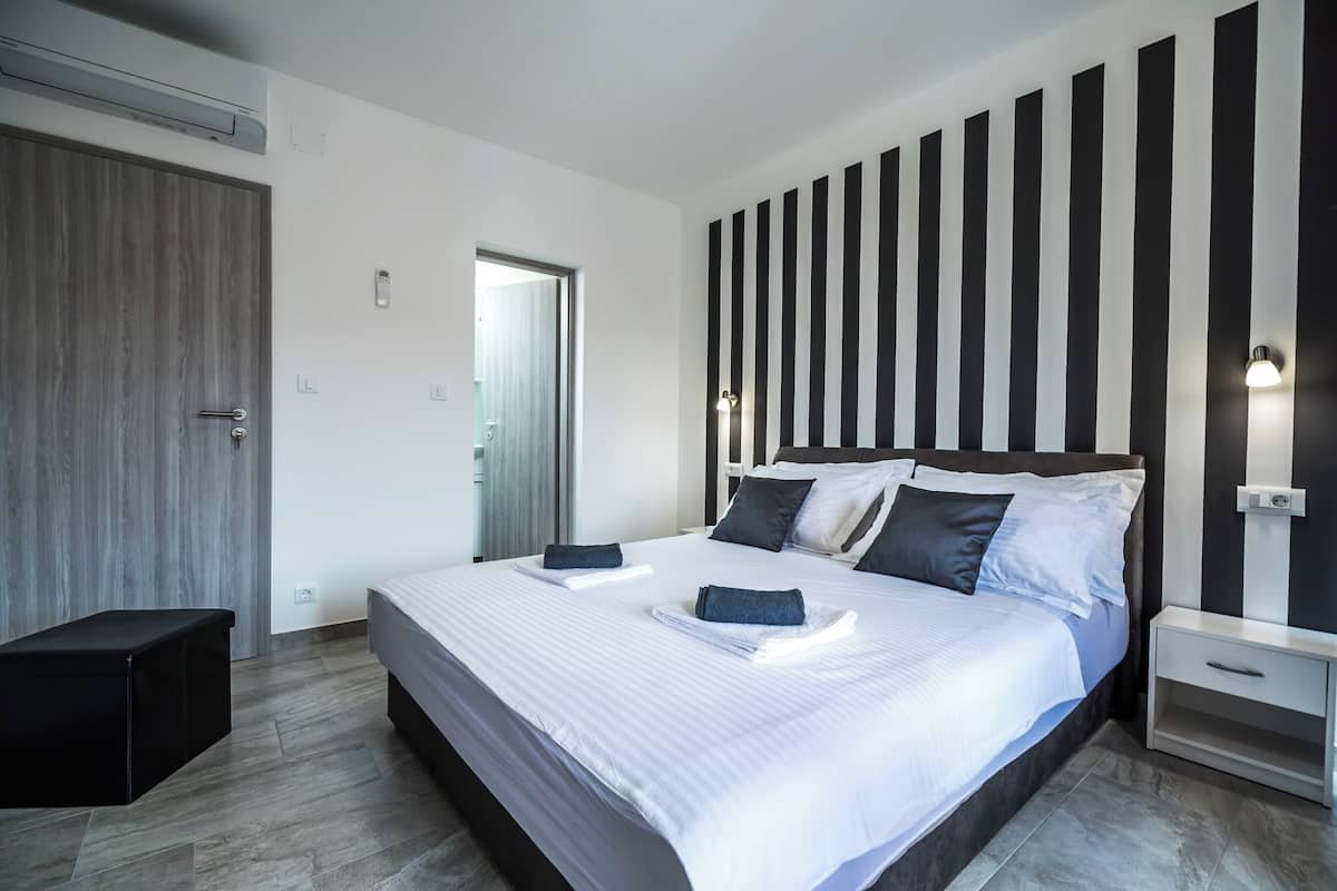 Ein modernes Schlafzimmer mit einem großen Bett, einem Nachttisch, einem Kleiderschrank und einem Streifenmuster an der Wand.