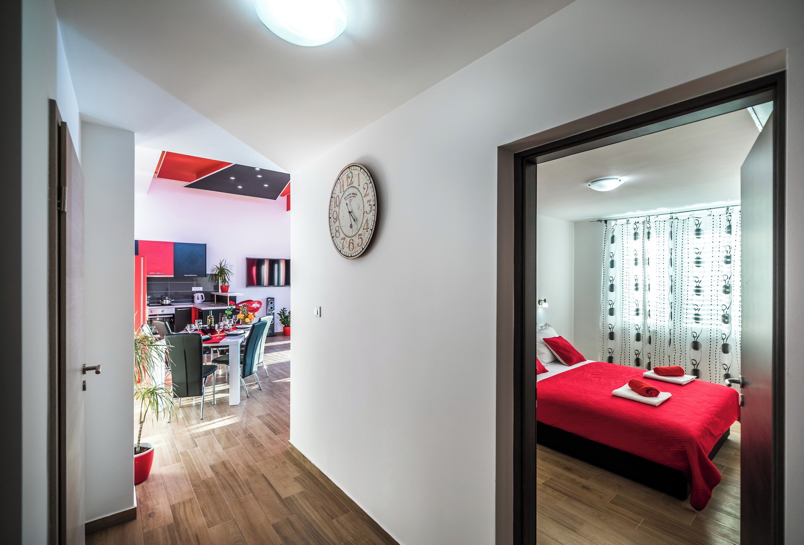 A modern hotel room with a large bed, a dining area, and a kitchen in the background.