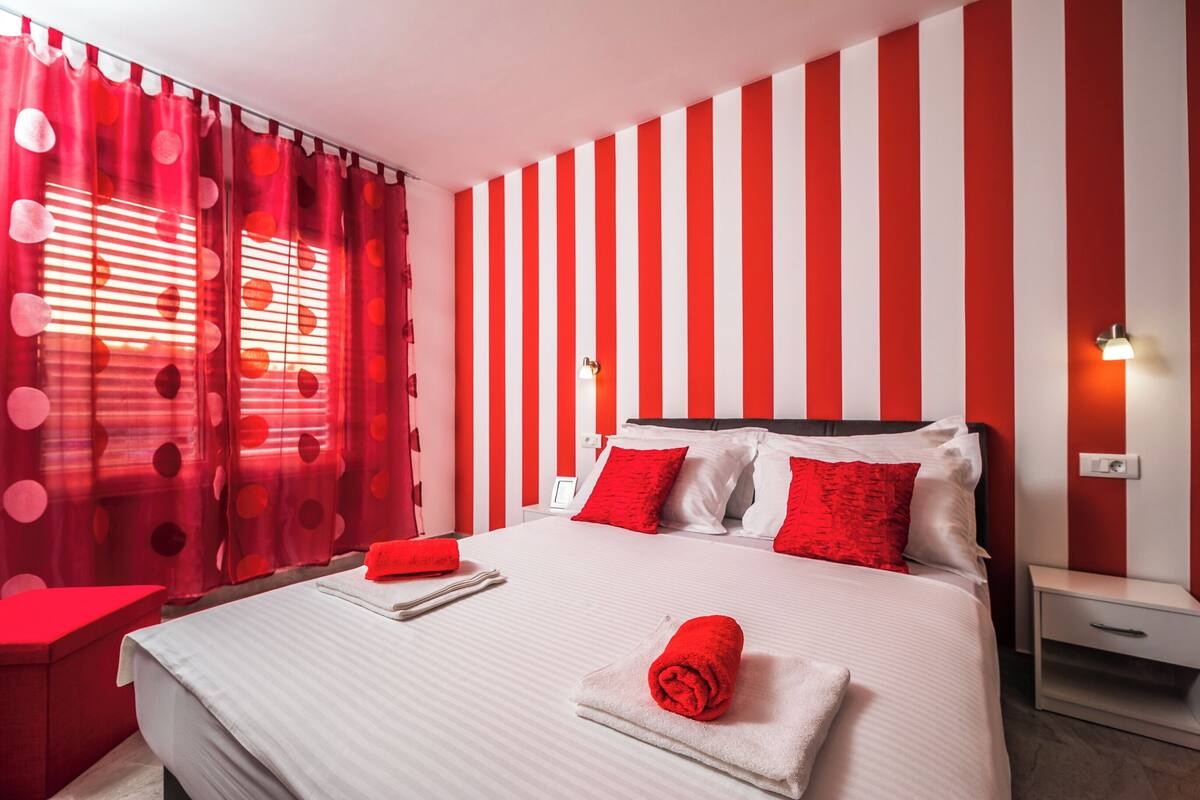 Ein Hotelzimmer mit einer rot-weiß gestreiften Wand, einem Bett mit rot-weißer Bettwäsche und einem roten Vorhang mit Punkten.