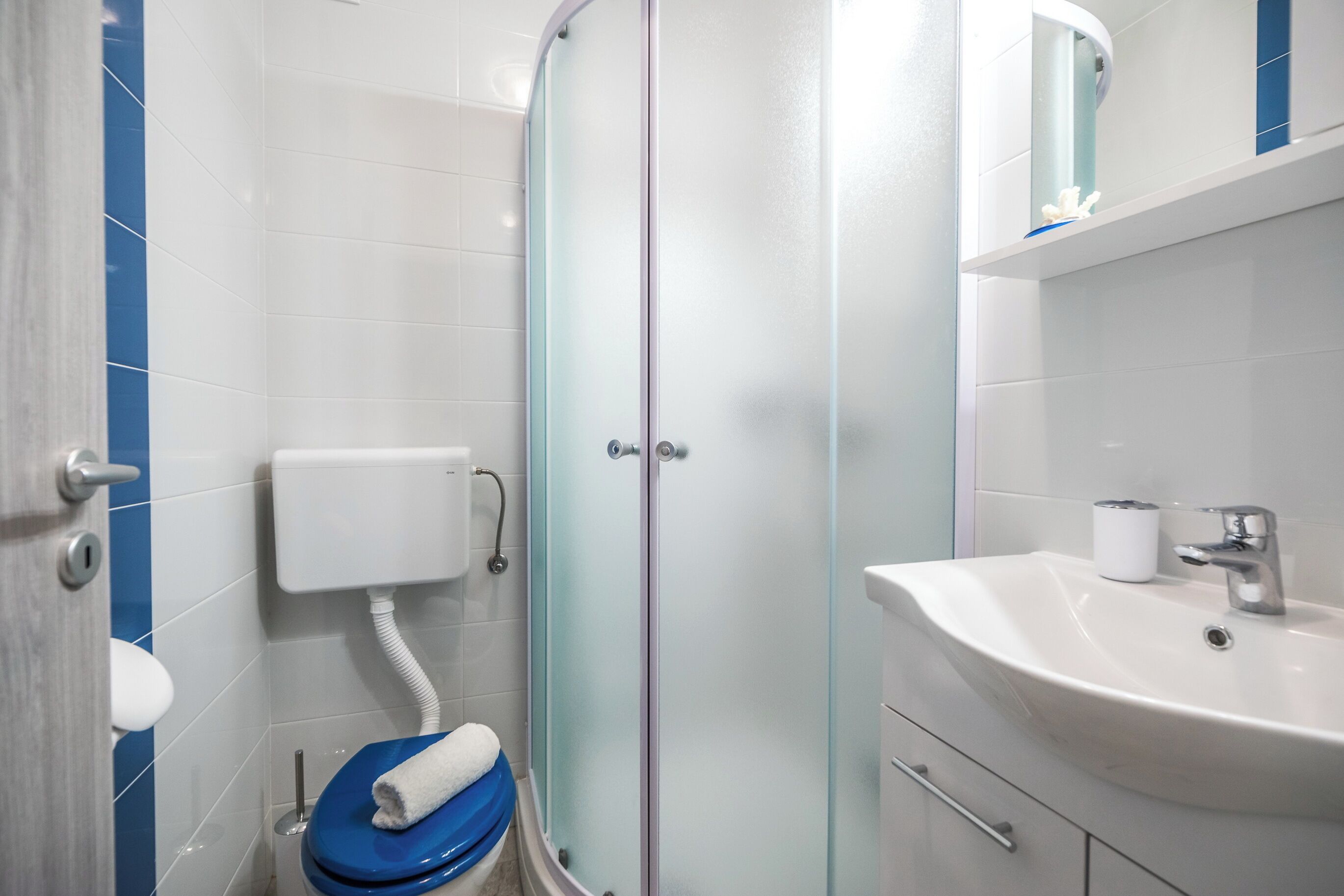 Ein Badezimmer mit Duschkabine aus Glas, einem weißen Waschbecken und einer blauen Toilette.
