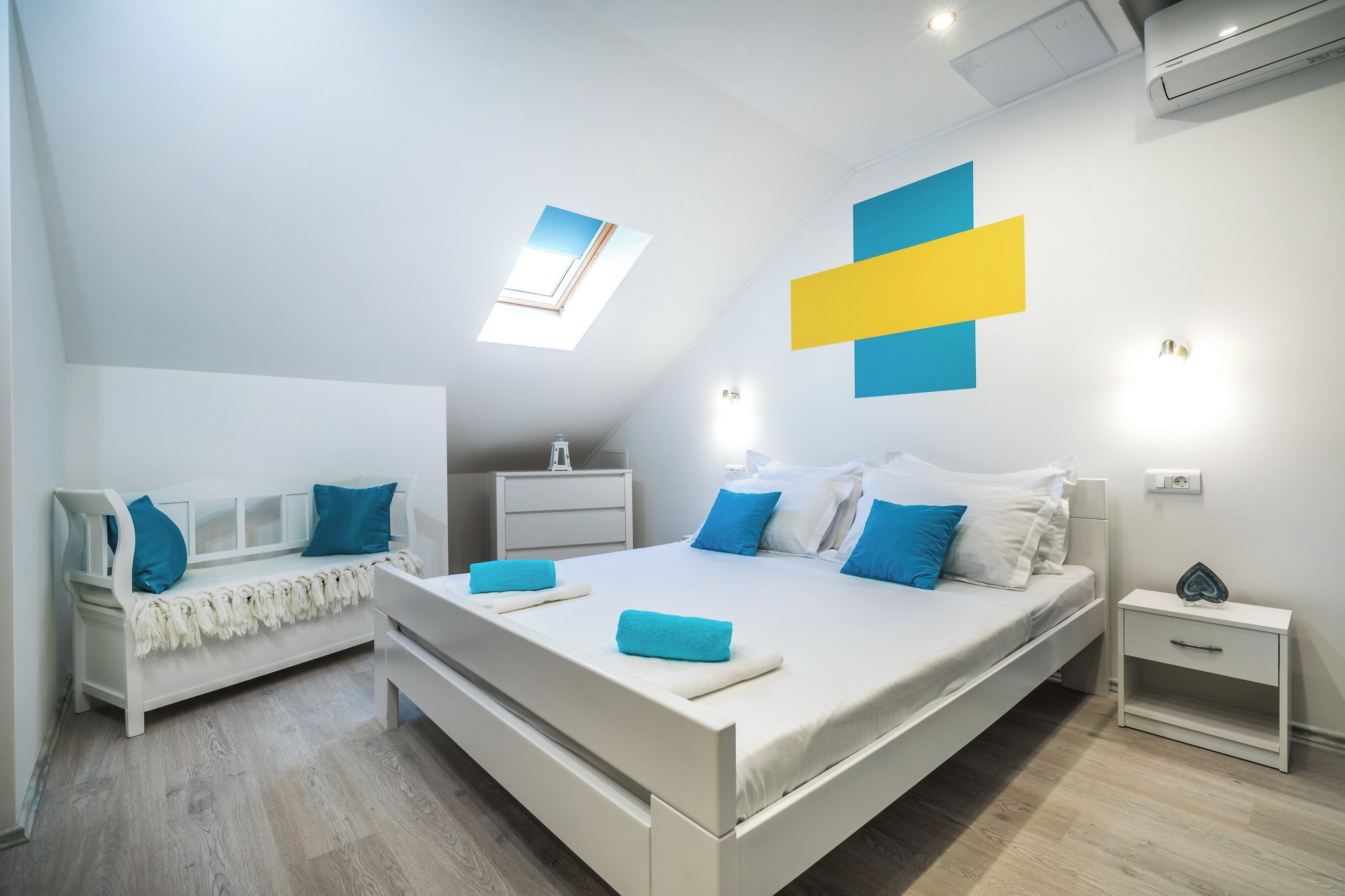 Un dormitorio moderno con una cama grande, una mesita de noche, un banco y un tragaluz.