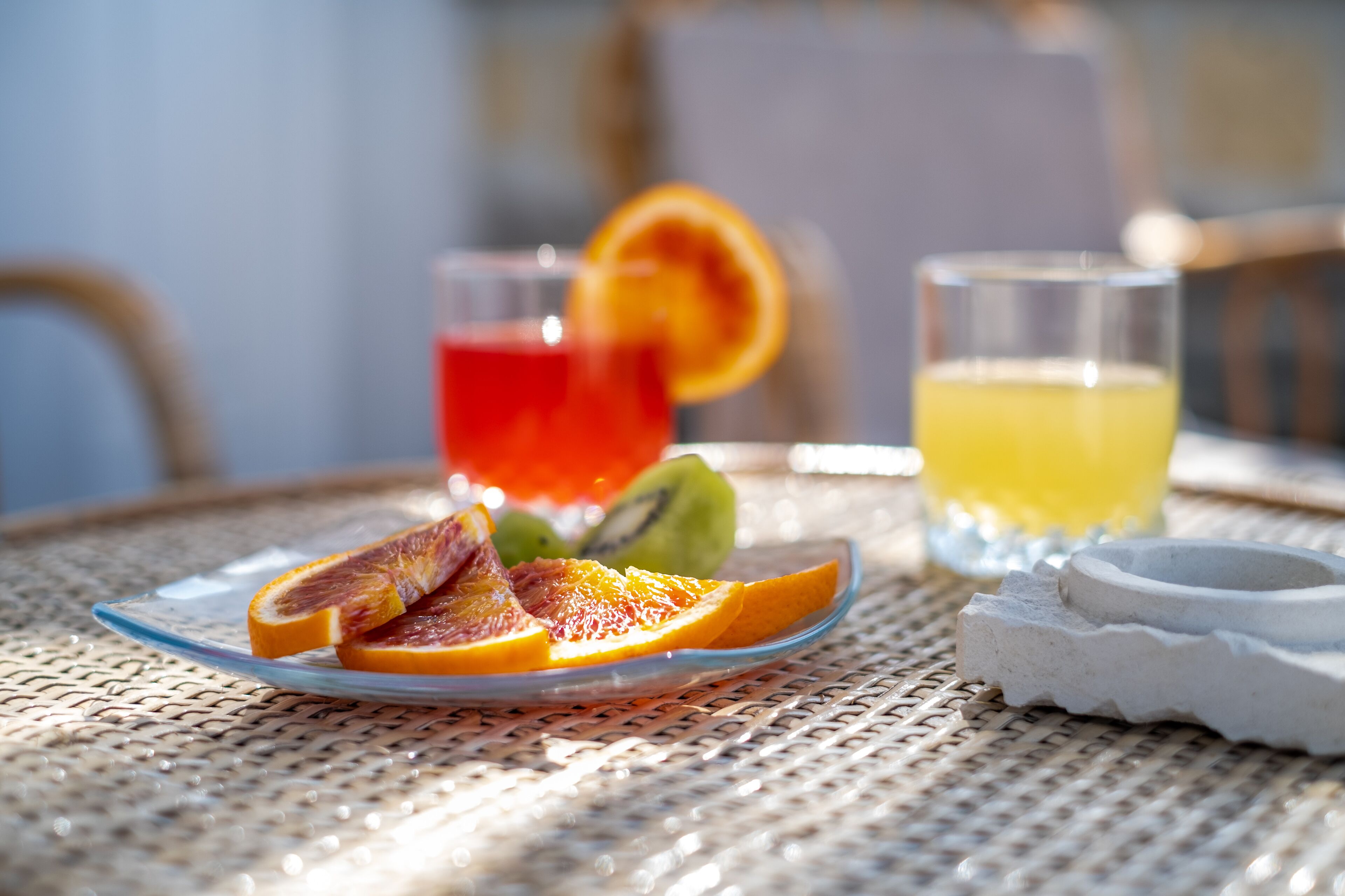 A table with a glass plate of sliced fruits, two glasses of beverages, and a small container.