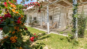 A wooden structure with a covered patio area, outdoor seating, and a garden with flowering plants. - Masseria Rauccio (Melendugno)