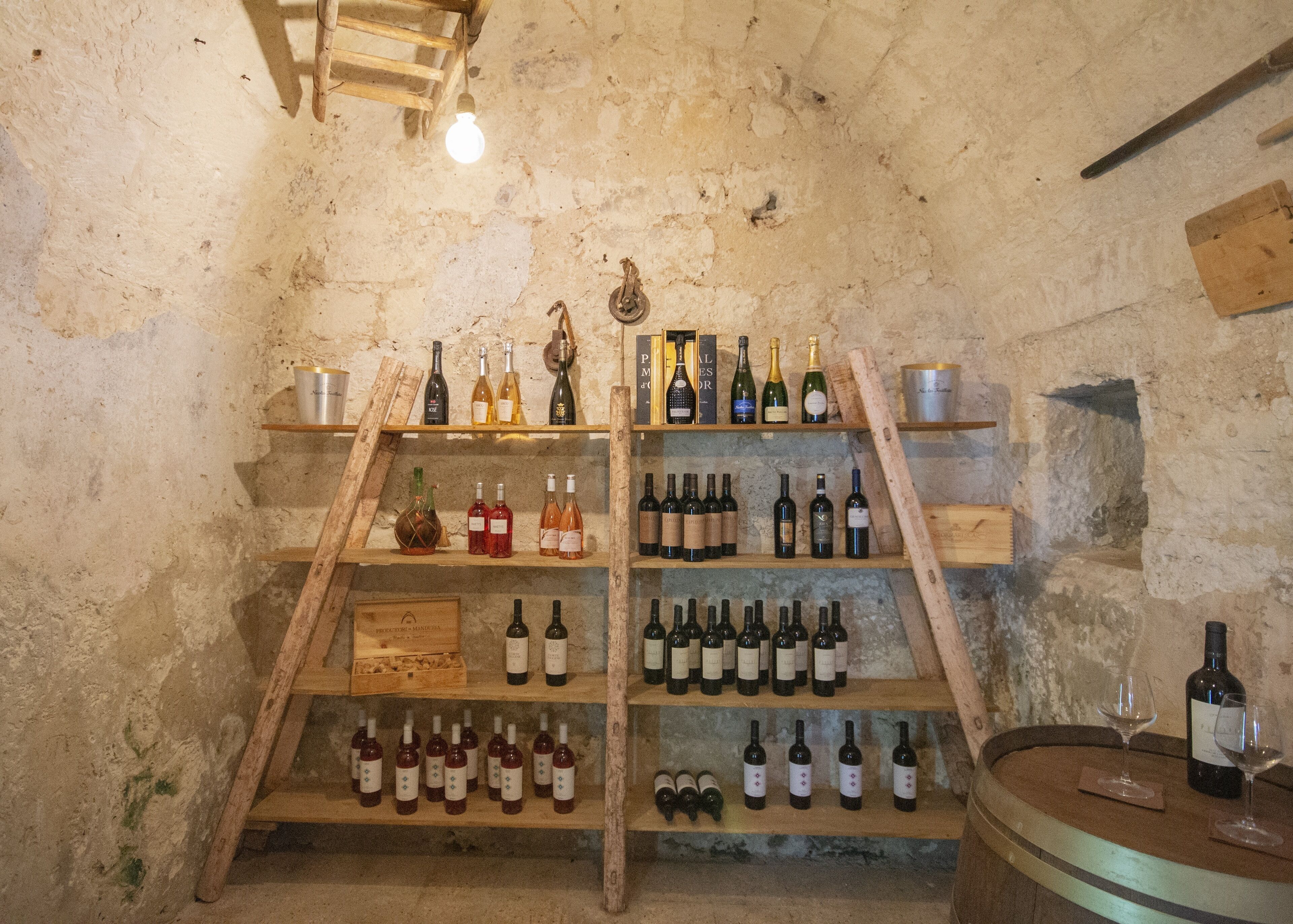 Una celler de vi amb prestatges de fusta on es mostren diverses ampolles de vi i unes quantes copes de vi.