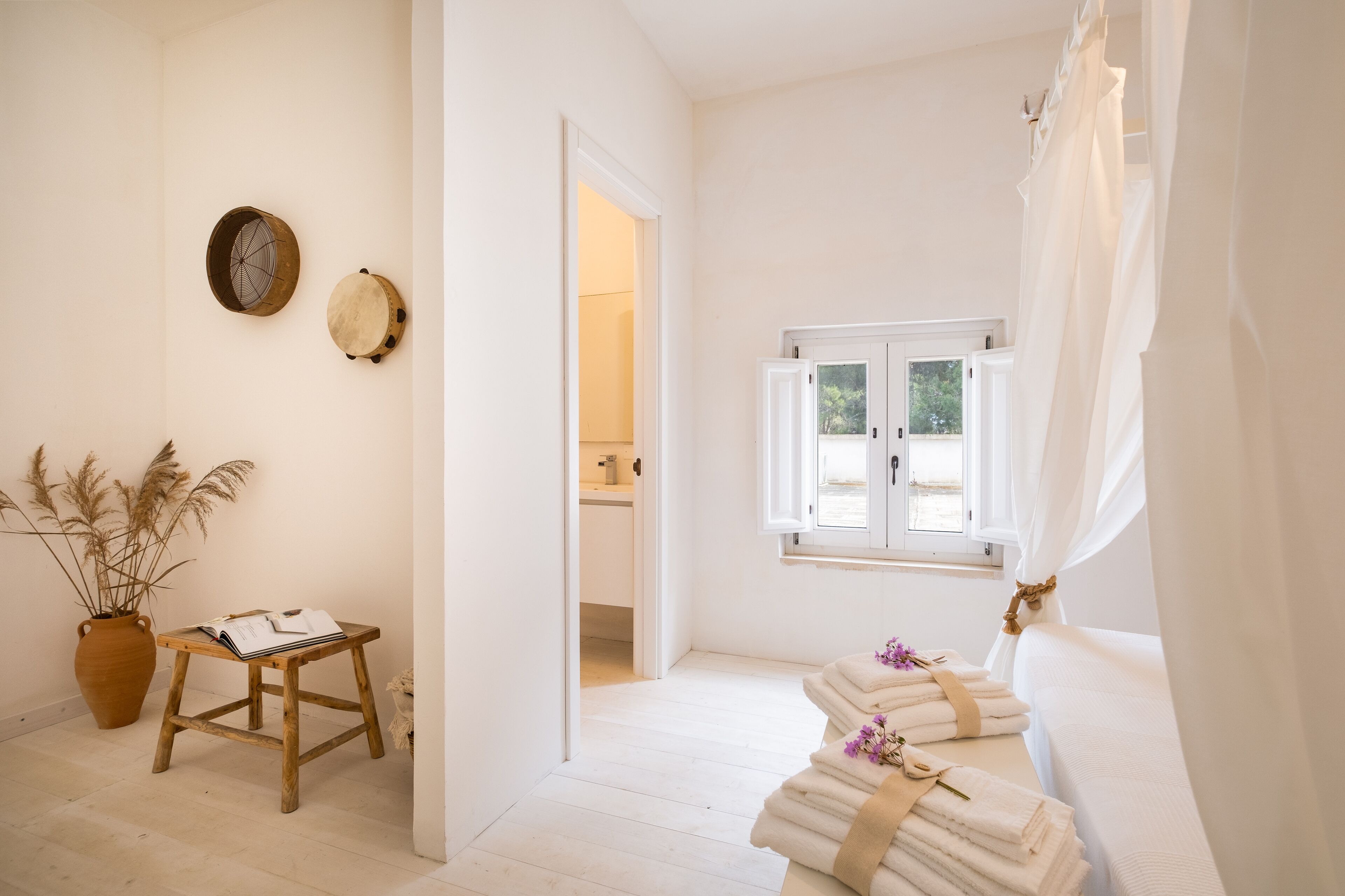 Un baño luminoso y minimalista con un ventanal grande, un taburete de madera y toallas en un tendedero.