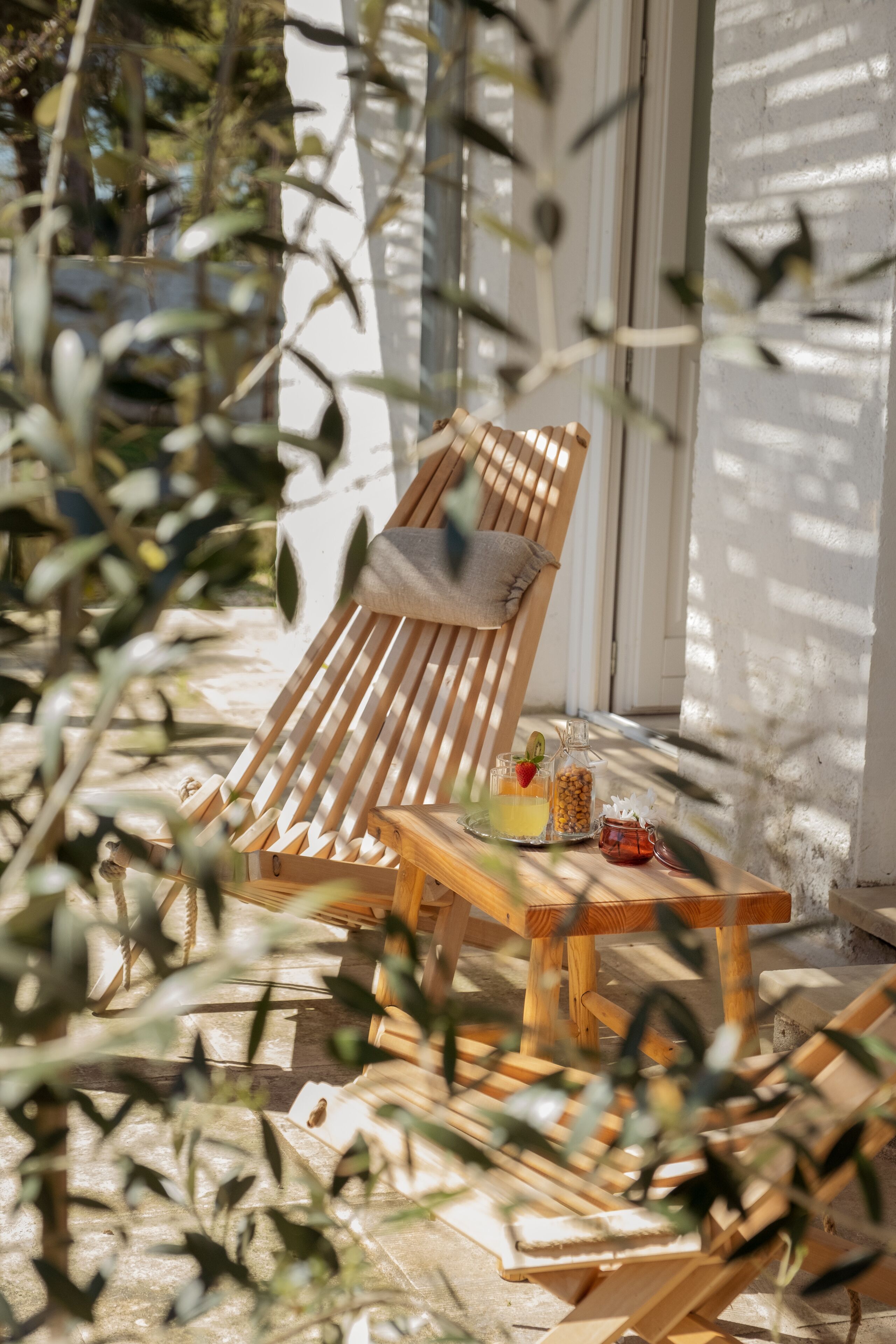 Un fauteuil de jardin en bois avec un coussin, une petite table avec des boissons et des en-cas, et un bocal en verre rempli de fruits secs.