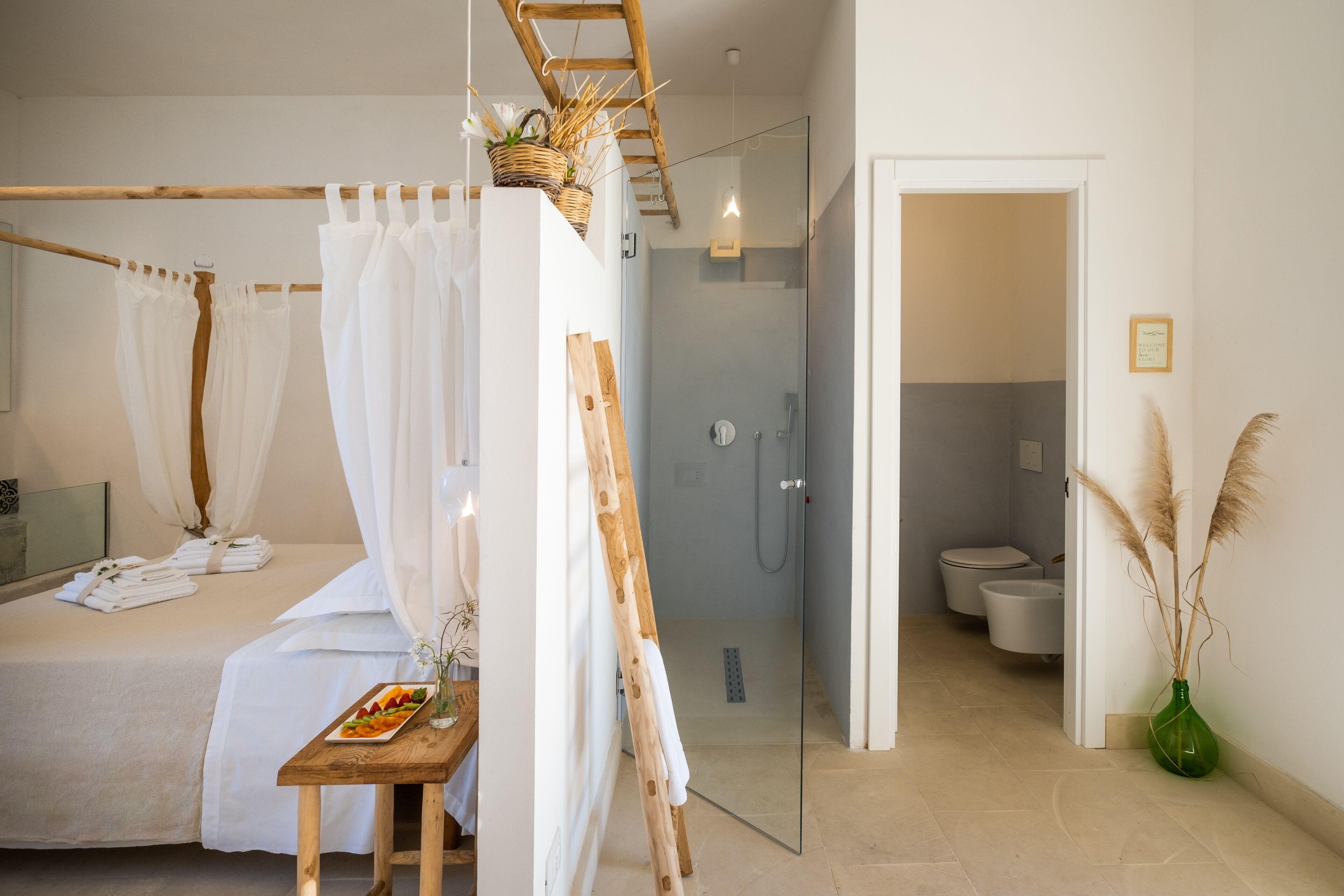 Et moderne soveværelse med en seng, en træstige, en glasbrusekabine og et badeværelse med toilet og håndvask.