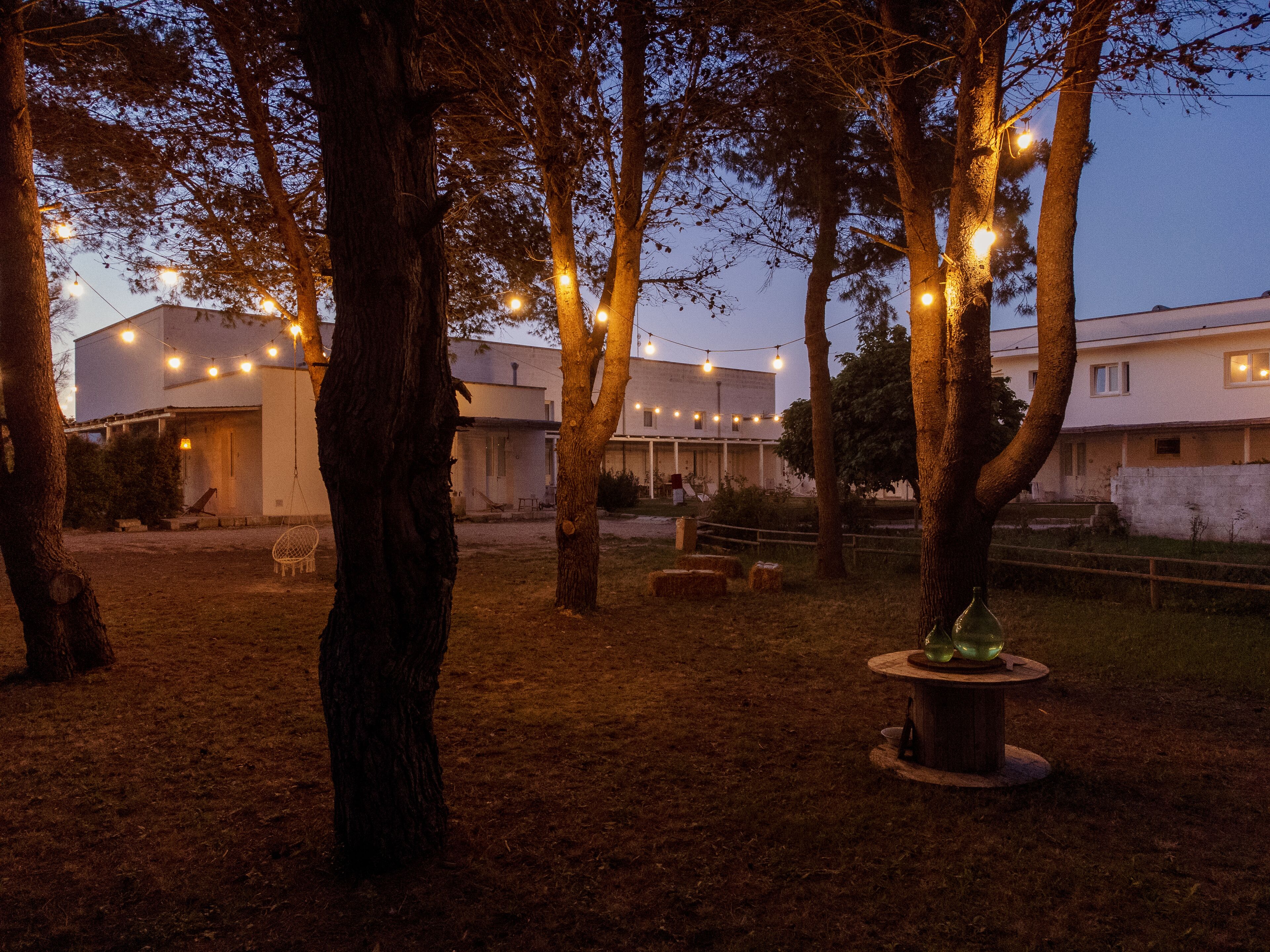 A courtyard with trees, hay bales, and string lights.