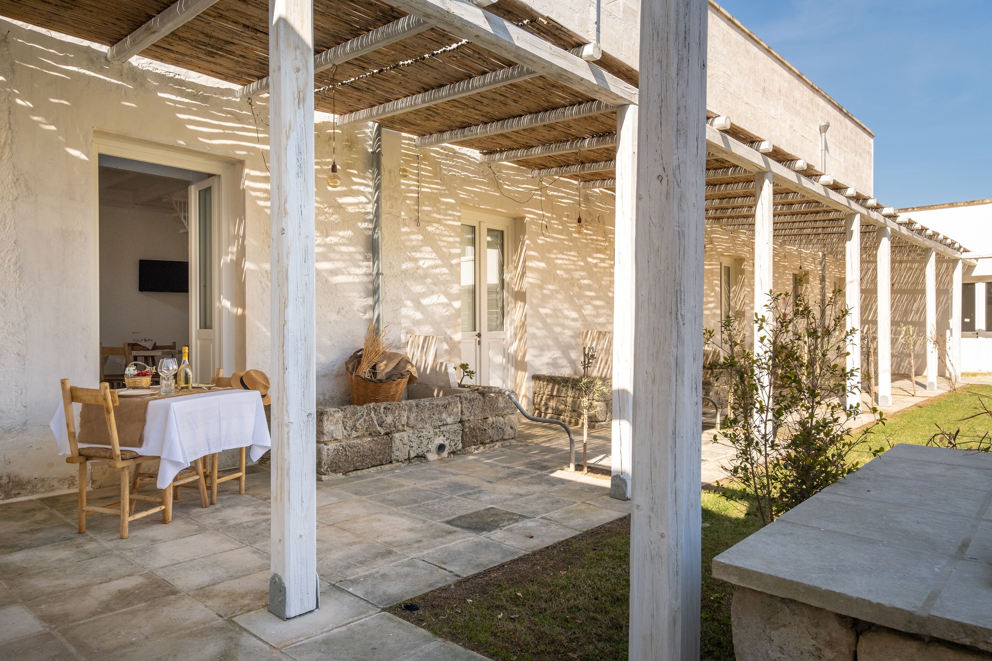 Un patio techado al aire libre con una mesa lista para comer, piso de piedra y una pared de piedra.